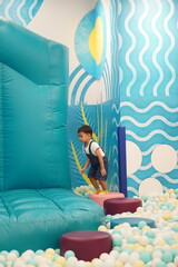 Naklejka premium Asian toddler boy standing in colorful ball pit at indoor playground