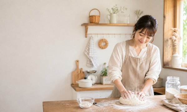 明るい自宅のキッチンで生地をこねながらパン作りを楽しむ笑顔の若い女性