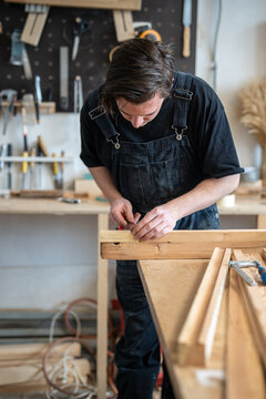 Woodworker precisely measuring wooden board replacement for vintage window frame at table, professional restorer holding ruler and making marks on planks with pencil, preparing parts for future repair