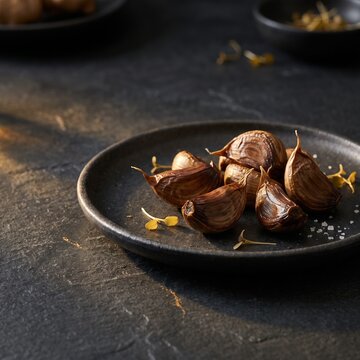 Close up of cloves of fermented black garlic served on a dark textured ceramic plate for a sophisticated gourmet culinary presentation