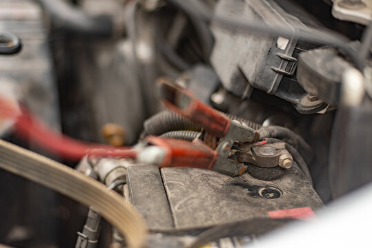 Close-up of red jumper cable clamping on dirty old car battery terminal for charging, real photography, not AI generated.