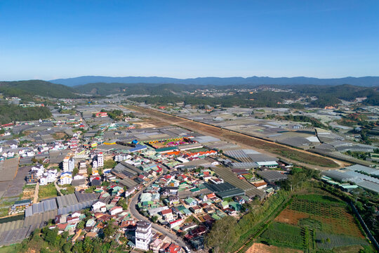 Aerial view showcases a lively town nestled in green hills, with colorful houses, sprawling farms, and fields stretching into the horizon under a clear blue sky