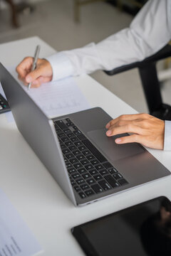 Asian businessman writing on document and typing on laptop