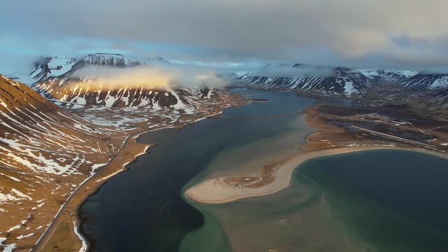 Aerial drone view of Skardsfjordur Fjord in the Westfjords Iceland featuring a curved sand spit calm bay snow patched mountains and rugged coastal landscape