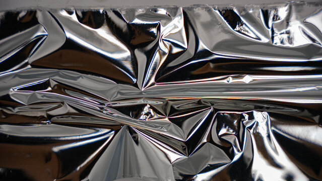 A horizontal sweep across wrinkled silver metallic material with smooth highlights and dark, recessed folds.