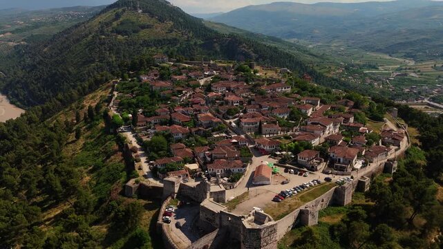 Wide aerial drone view showcasing the historic hilltop settlement and ancient fortifications of Berat Castle surrounded by lush valleys in Albania