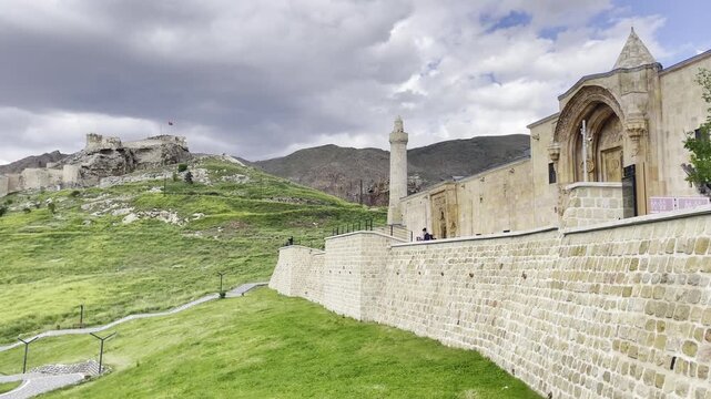 Wide exterior view of the historic stone walls and lush green surroundings of the Great Mosque of Divriği in Sivas, Turkey