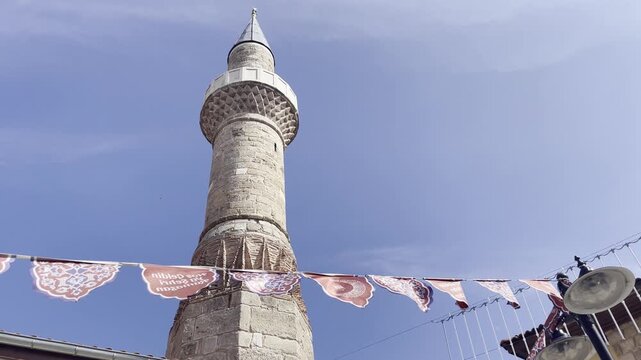 Low-angle upward view of a historic minaret tower decorated with festive string flags against a bright clear sky in Antalya, Turkey