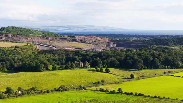 Cinematic aerial view, Operational quarry site on the west coast of Scotland, showing earthworks, aggregate stockpiles and surrounding woodland