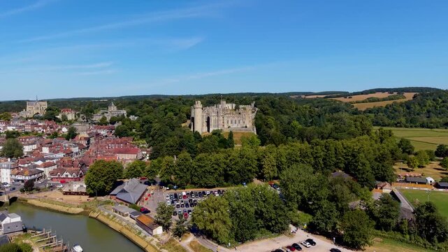Arundel Castle drone ascent from afar reveals Arundel town to the left, River Arun waterfront, and surrounding countryside on a clear summer day in West Sussex, England.