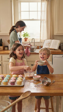 Mother and two children are baking cupcakes in a cozy kitchen.