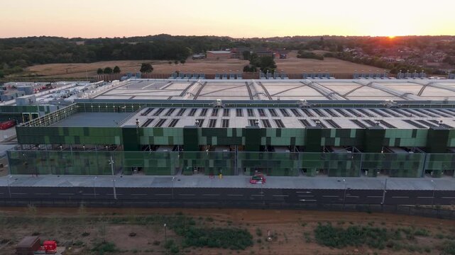 Google data centre, Waltham Cross, England. Right pan aerial view of large campus building at sunset, golden hour light with sun low on the horizon behind.