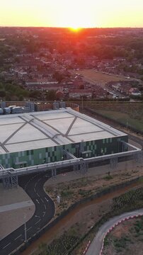 Google data centre Waltham Cross at sunset as drone reverses and pans left over the campus, revealing rooftops, service roads and surrounding fields with the sun on the horizon. Vertical format.