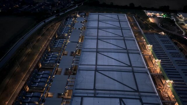 Google data centre, Waltham Cross at dusk in reverse pan over rooftop structure, perimeter lights and industrial plant, highlighting always-on energy use, light pollution and carbon footprint concerns