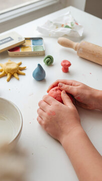 Hands of a child working with colorful modeling clay to create different shapes.