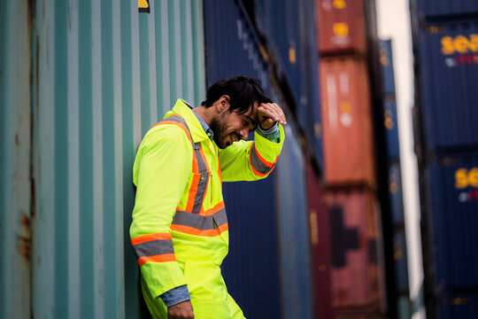 Stressed container yard engineer holding forehead experiencing headache and overwork.  Workplace Stress, Heat Stress, Problem Solving, System Delay, Industrial Crisis