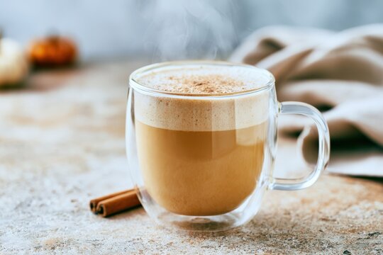 Transparent double wall glass cup filled with creamy pumpkin spice latte and cinnamon stick beside