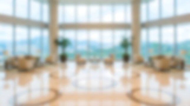 Blurred view of an expansive office lobby with white armchairs and glass windows looking out at a mountain landscape in a bright airy professional corporate building environment setting