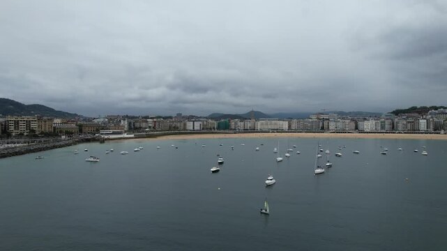 Aerial view of La Concha Bay with boats anchored in the calm water and the urban skyline along the beach in Donostia San Sebastian, Basque Country, Spain.