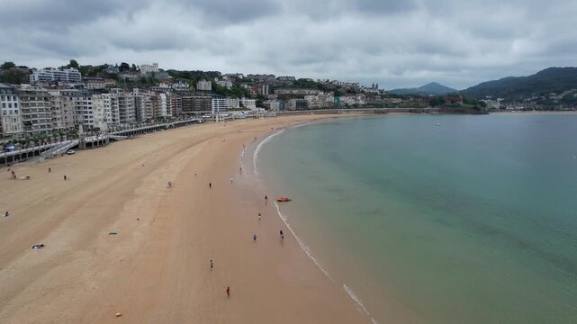Aerial view of La Concha Beach with golden sand and calm turquoise waters under a cloudy sky in Donostia San Sebastian, Basque Country, Spain.