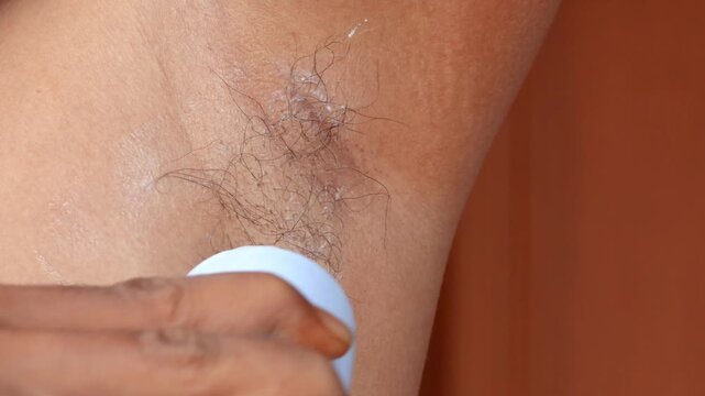 Close-up of Asian man applying antiperspirant deodorant to his underarm as part of a male hygiene routine and daily personal care at home.
