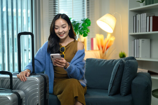 Young Woman with Luggage Using Smartphone on Sofa, Planning Travel Trip at Home