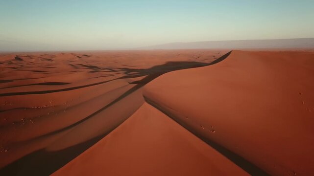 Aerial view of vast orange sand dunes of the Sahara Desert under a clear sky in Morocco.