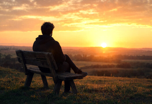 Silhouette of a person sitting on a bench watching a beautiful sunset over countryside landscape