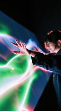 South Asian woman reaching toward a glowing digital interface with vivid light trails and colorful projections for technology and business concepts
