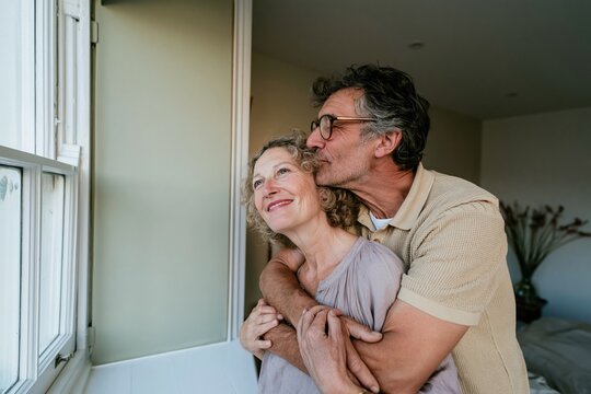 Middle-aged couple embracing by a bedroom window, featuring soft knit textures and a calm, natural mood for relationship and wellbeing marketing