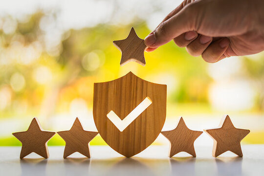 Hand placing wooden star above shield icon with checkmark for top quality service rating five stars guarantee customer satisfaction policy concept.