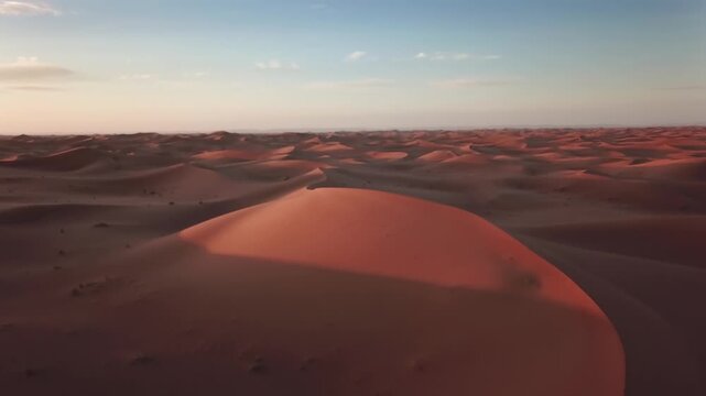 Aerial view of rolling sand dunes of the Sahara Desert under a clear sky at sunset in Morocco.