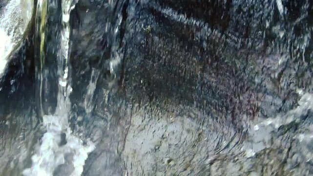 Close up of crystal clear mountain stream water pouring over dark wet rocks