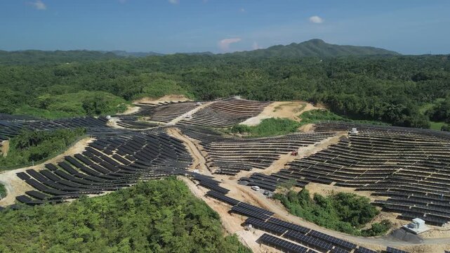 Drone ascends over hillside solar panel arrays, access roads, and surrounding forest at Sikatuna Solar Power Plant in Bohol