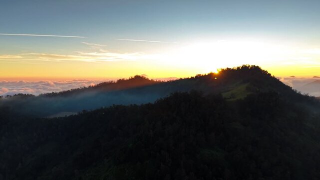 Aerial view of Dieng Plateau at sunrise with mist rolling over the forested mountains in Indonesia.