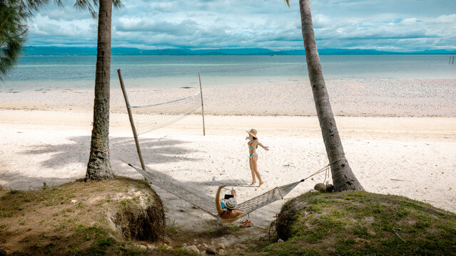 Top view of couple tourist are in motion of relaxing stay under coconut palm tree at the the edge of the sea beach,  trip summer on vacation of couple lover