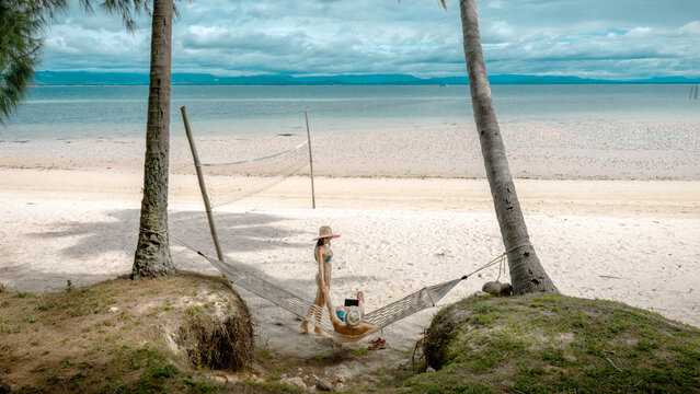 Top view of couple tourist are in motion of relaxing stay under coconut palm tree at the the edge of the sea beach,  trip summer on vacation of couple lover