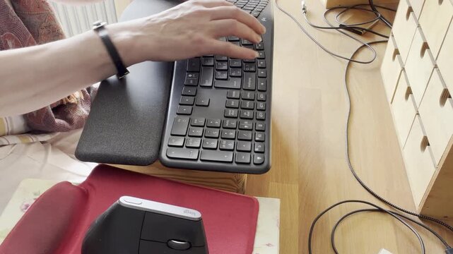 Female hands typing on an ergonomic keyboard beside a computer mouse on a clean beech wood desk in a modern workspace. Static Shot.