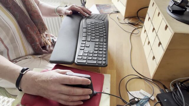 Female hands moving a computer mouse on a red mouse pad while typing on an ergonomic keyboard at a wooden desk. Static Shot.