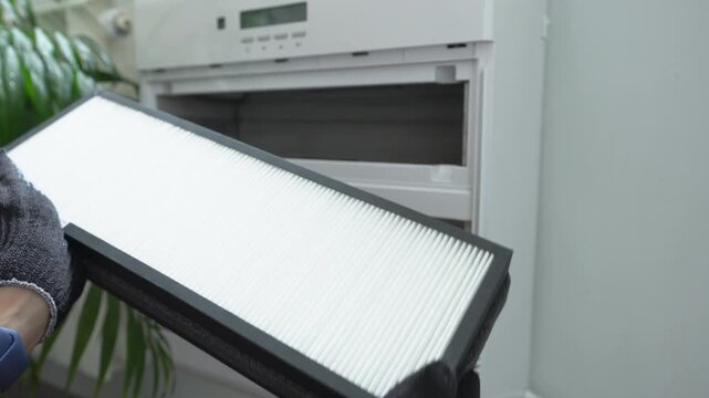 A person holding a new air filter for an air purification system. A person wearing gloves holds a new air filter.
