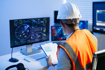 Obraz na płótnie Canvas Industrial engineer in a safety helmet and reflective vest monitors digital dashboards and control systems, combining technology, data analysis, workplace safety and modern industry.
