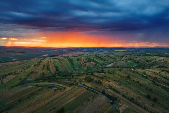 Aerial view of rolling agricultural fields under a dramatic sunset sky with storm clouds in Mutenice, South Moravian Region, Czechia.
