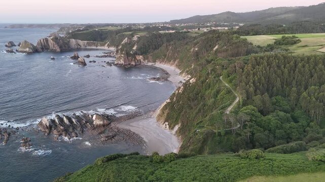 Wide aerial panorama of secluded beaches, dramatic sea stacks, green cliffs and forest along the Asturian coast.