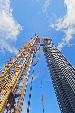 Drilling rig with top drive system (TDS) during tripping in the drill pipe to drill the hole in crude oil exploration operation with sunny blue sky background. Heavy industrial working scene.