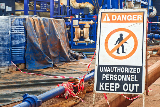 Danger, keep out sign with high-pressure pumping unit as background. Using to barricade hazard working area at industrial working site. Sign and symbol for industrial workplace, close-up.