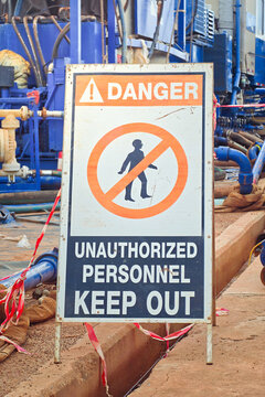 Danger, keep out sign with high-pressure pumping unit as background. Using to barricade hazard working area at industrial working site. Sign and symbol for industrial workplace, close-up.