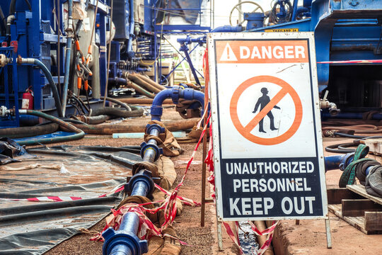 Danger, keep out sign with high-pressure pumping unit as background. Using to barricade hazard working area at industrial working site. Sign and symbol for industrial workplace, close-up.