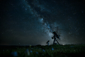Fototapeta premium Silhouette of an astronomical telescope positioned on a dark grassy hill under a vast night sky with the glowing milky way galaxy visible