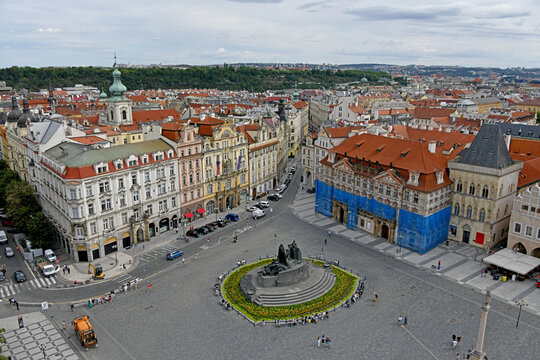 Elevated view of Prague's Old Town Square highlighting the Jan Hus Memorial at its center, surrounded by historic pastel facades and red-tiled roofs.