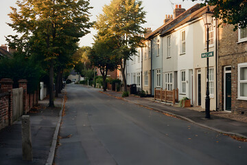 Fototapeta premium Quiet suburban street with traditional houses and trees at sunset with a maple lane sign on a lamp post in the foreground
